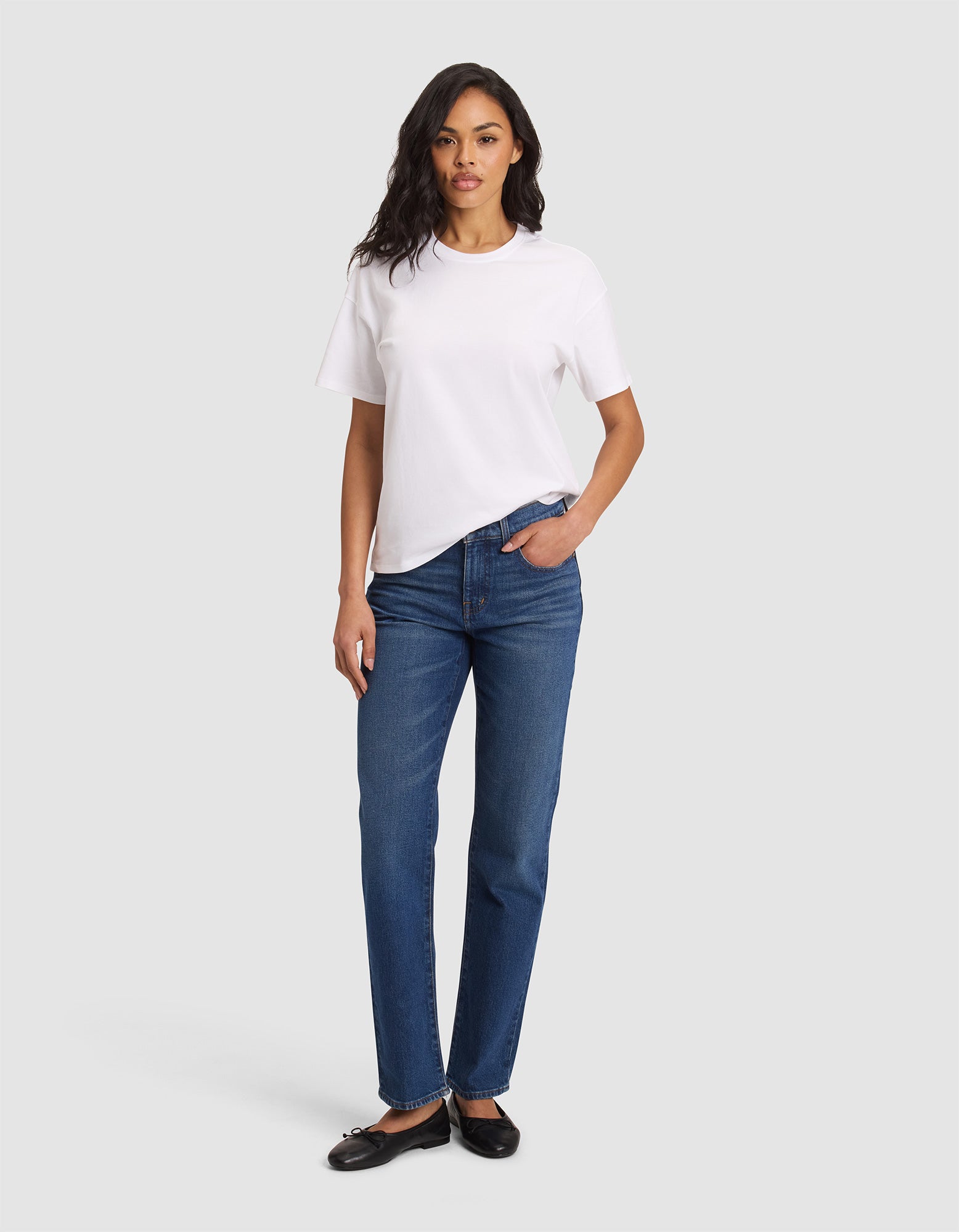 A woman stands facing forward in the Cozy Earth Women's All Day Tee, paired with blue jeans and black flats. She has one hand in her pocket and a neutral expression, set against a plain light gray background. 