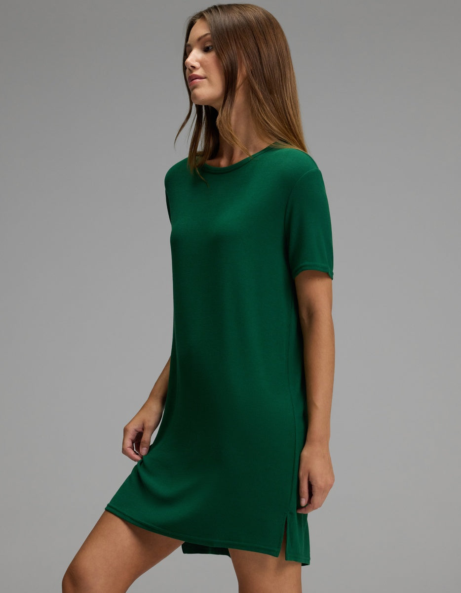 A woman models the Cozy Earth Women’s Bamboo Rib-Knit Boyfriend Sleep Dress, a short-sleeve, knee-length green dress, standing against a plain gray background and facing slightly to the left with her arms relaxed at her sides.