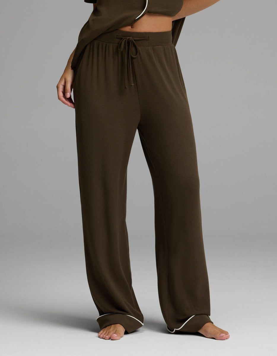 A person is shown from the waist down, standing barefoot on a gray background, wearing Cozy Earth’s Women’s Bamboo Rib-Knit Classic Pajama Pant in brown with a comfortable drawstring waist.