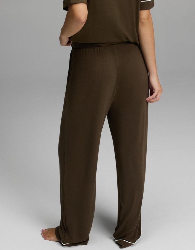 A person standing barefoot, shown from the waist down, wearing Cozy Earth’s Women’s Bamboo Rib-Knit Classic Pajama Pant in brown with a matching short-sleeve top against a plain background.