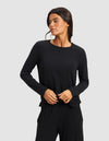 A woman with long dark hair wears the Cozy Earth Women’s Bamboo Rib-Knit Long Sleeve Lounge Top in black, paired with matching black pants, standing against a plain light gray background and looking to her left.|Color:Black