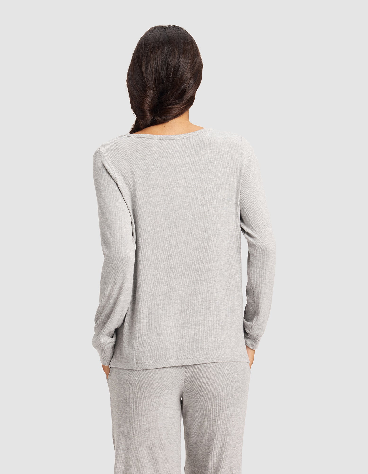 A woman with long dark hair in a loose braid is shown from the back, wearing the Cozy Earth Women’s Bamboo Rib-Knit Long Sleeve Lounge Top in light gray against a plain light gray background.