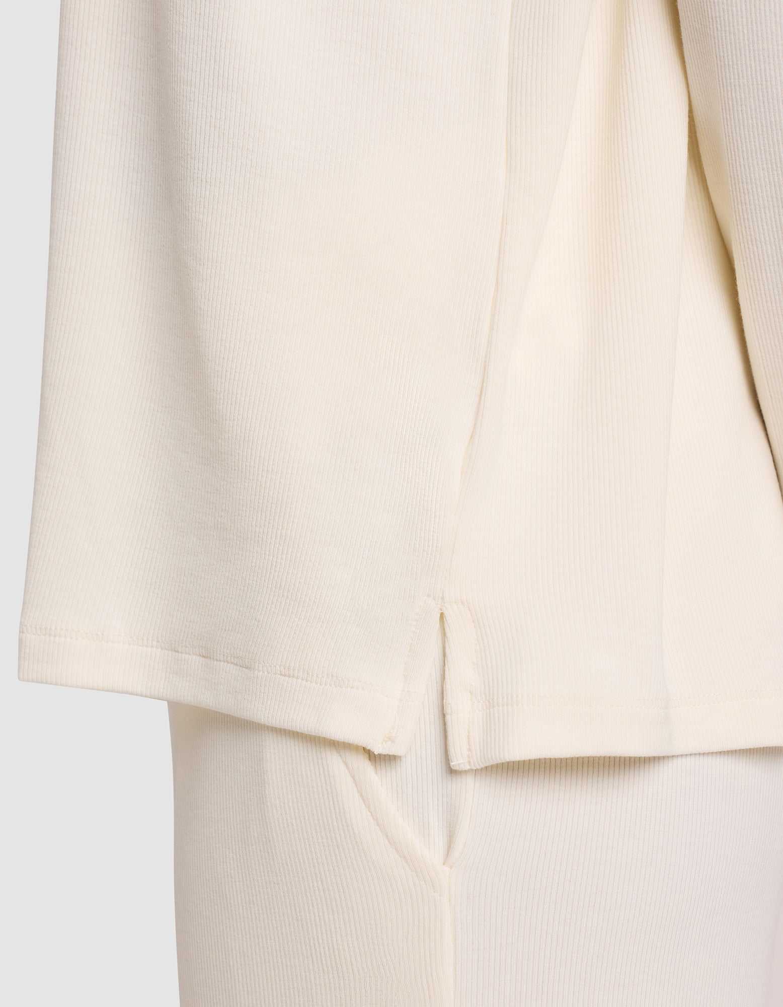Close-up of Cozy Earth’s Women’s Bamboo Rib-Knit Long Sleeve Lounge Top in cream, showing the hem with a side slit over matching pants. The ribbed texture and stitching details highlight the soft bamboo fabric.