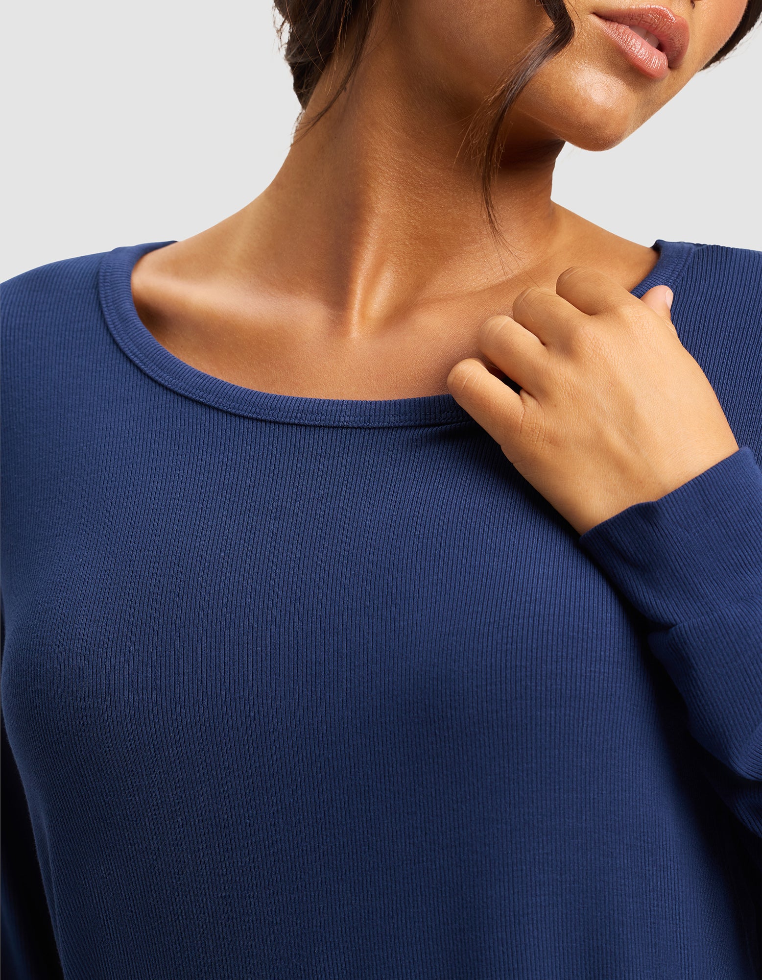 A woman wears the Cozy Earth Women’s Bamboo Rib-Knit Long Sleeve Lounge Top in dark blue, lightly touching her collarbone. The cropped image highlights her neck, shoulders, and upper chest.