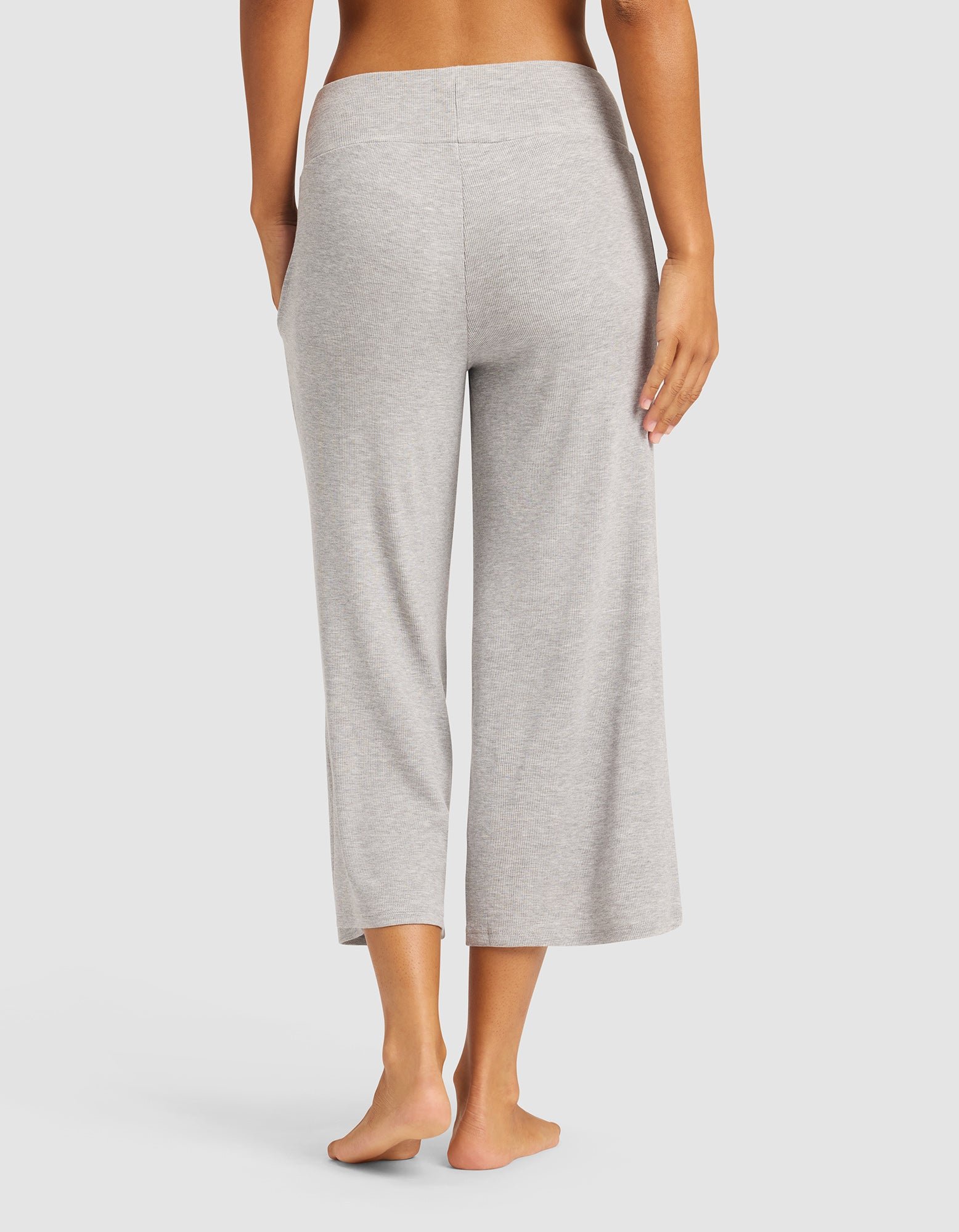 A woman stands barefoot facing away from the camera, wearing Cozy Earth's Women’s Bamboo Rib-Knit Lounge Capri in light gray against a plain white background.