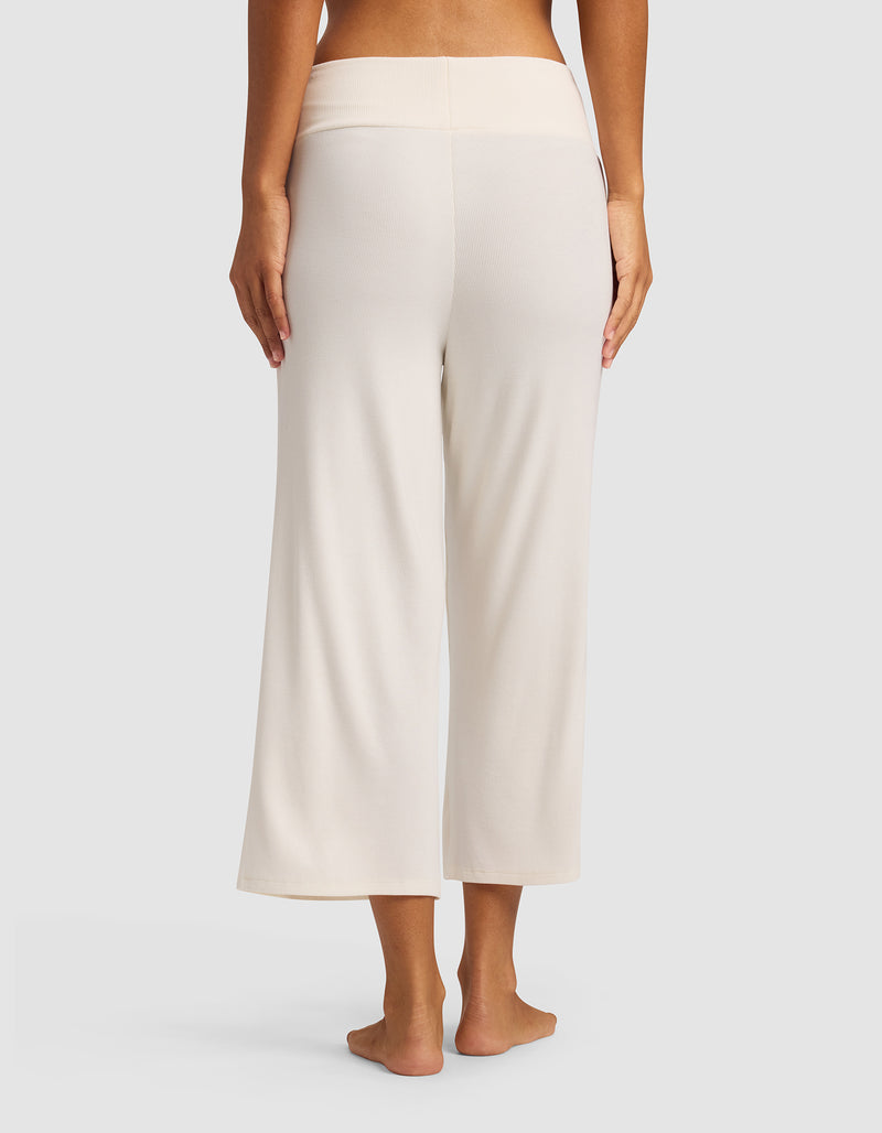 A person stands barefoot on a light surface, shown from the back, wearing Cozy Earth Women’s Bamboo Rib-Knit Lounge Capri in cream with a matching waistband.