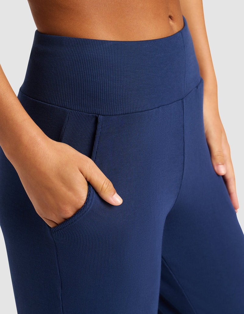 A person wears Cozy Earth’s Women’s Bamboo Rib-Knit Lounge Pant in navy blue, with one hand in their pocket, highlighting the high-waisted ribbed waistband and pocket detail.