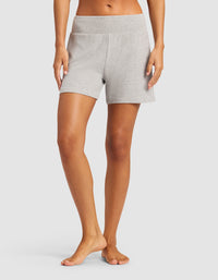 A person stands barefoot, shown from the waist down, wearing light gray Cozy Earth Women’s Bamboo Rib-Knit Lounge Shorts with a matching waistband against a plain white background.|Color:Grey