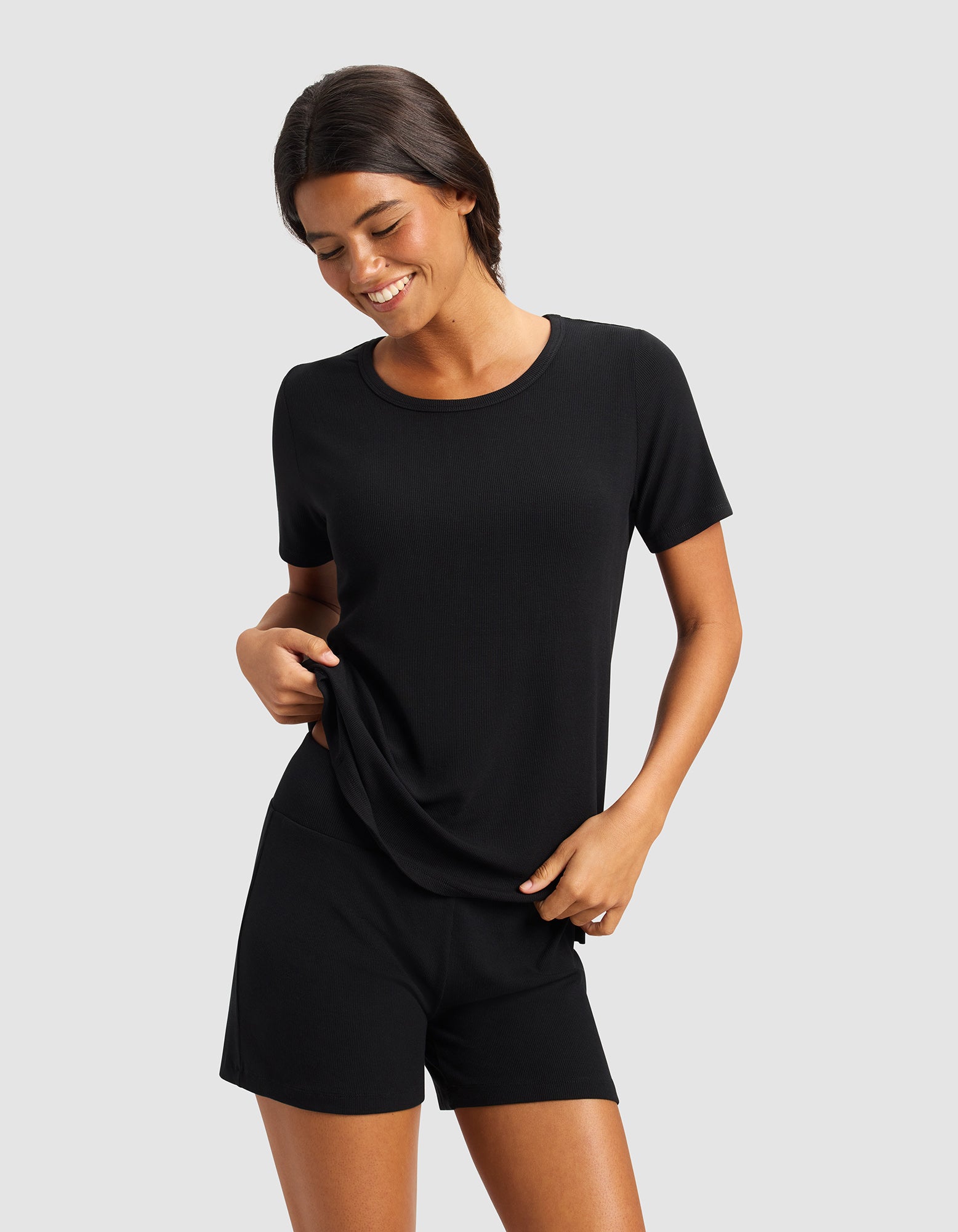 A dark-haired woman smiles and looks down against a light background, wearing the Cozy Earth Women’s Bamboo Rib-Knit Short Sleeve Lounge Top in black.