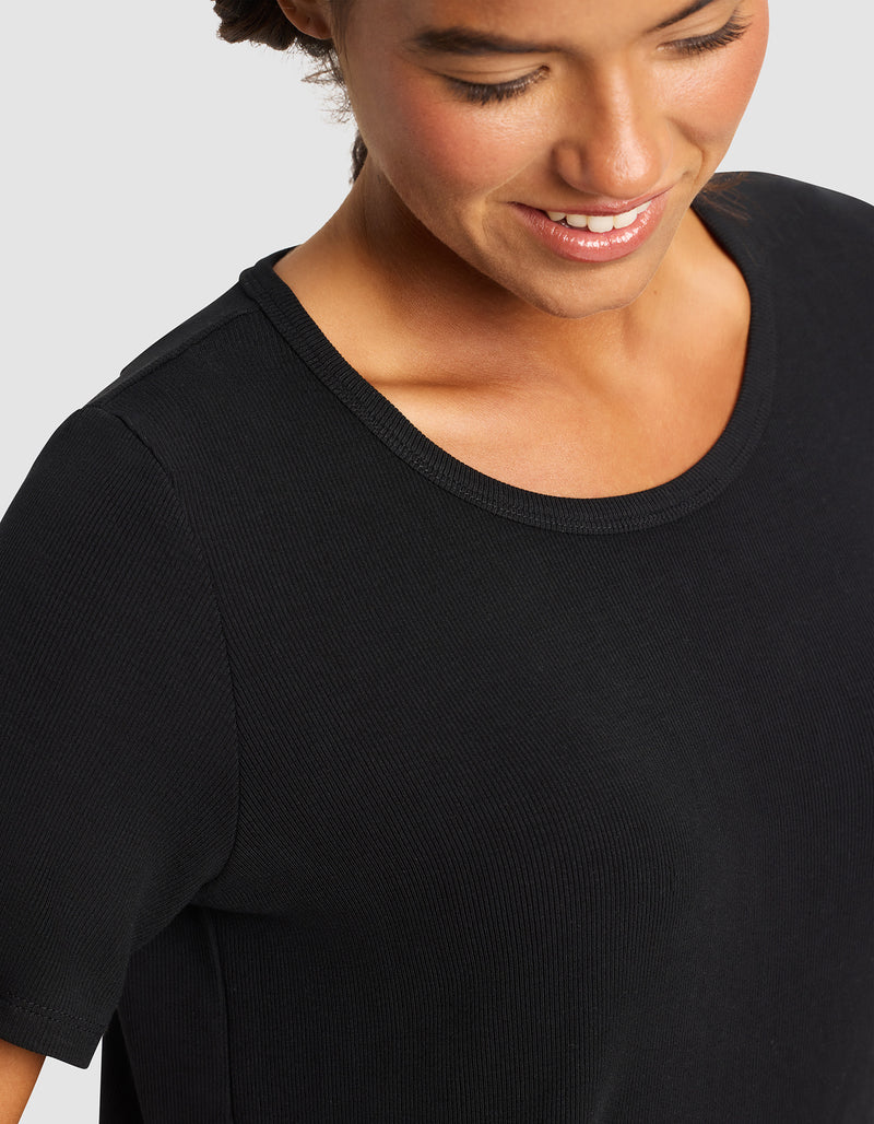 A woman smiles and looks down, wearing the Cozy Earth Women’s Bamboo Rib-Knit Short Sleeve Lounge Top in black against a plain light background.