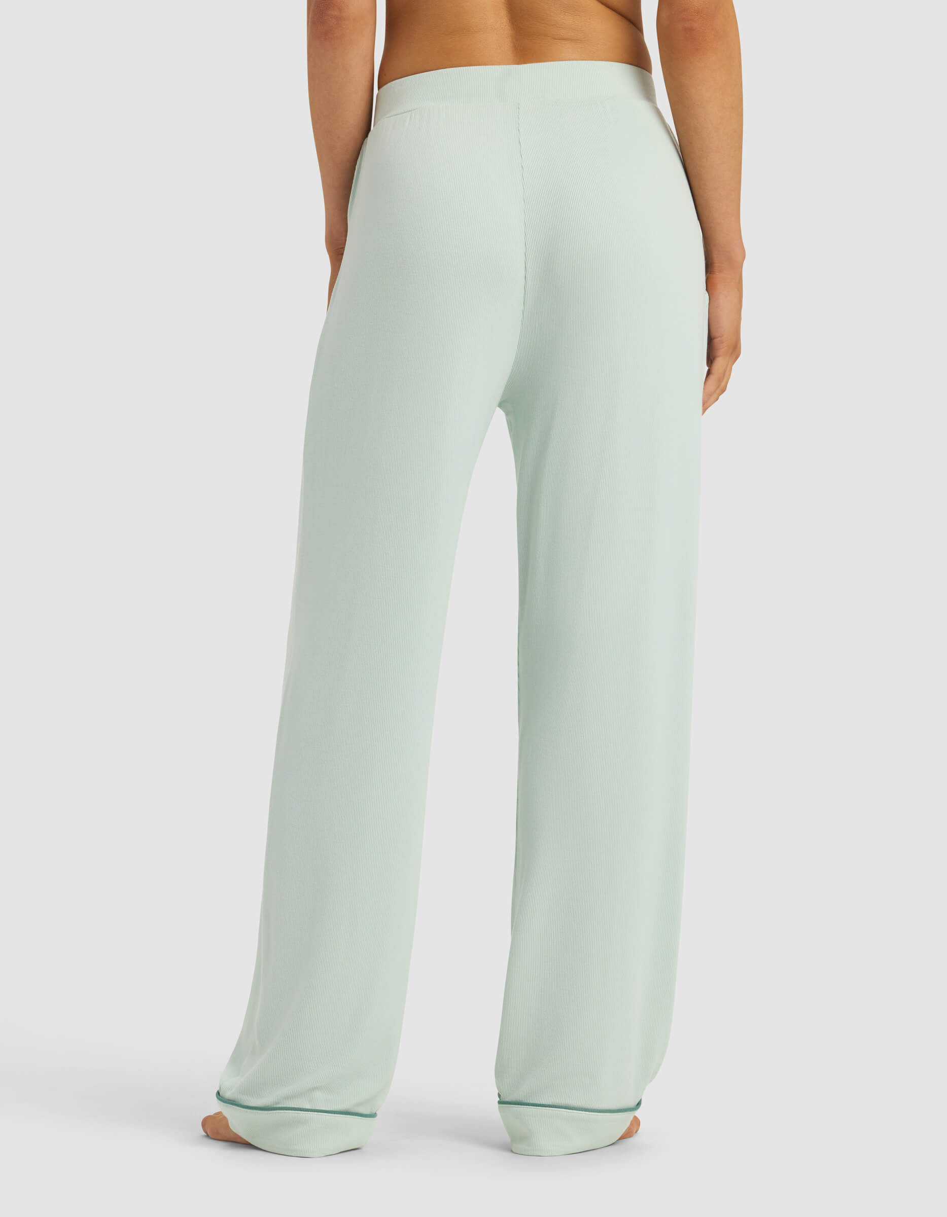 A person is shown from the back wearing Cozy Earth's Women's Bamboo Rib-Knit Classic Pajama Pant in light mint green with a relaxed fit and wide legs, standing barefoot on a plain white background.|Color:Seafoam