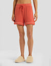 A person is seen from the waist down wearing Cozy Earth Women's Bamboo Rib-Knit Classic Pajama Shorts in coral, featuring a drawstring and rolled hems, paired with cream fuzzy slippers against a plain light gray background.|Color:Sunset