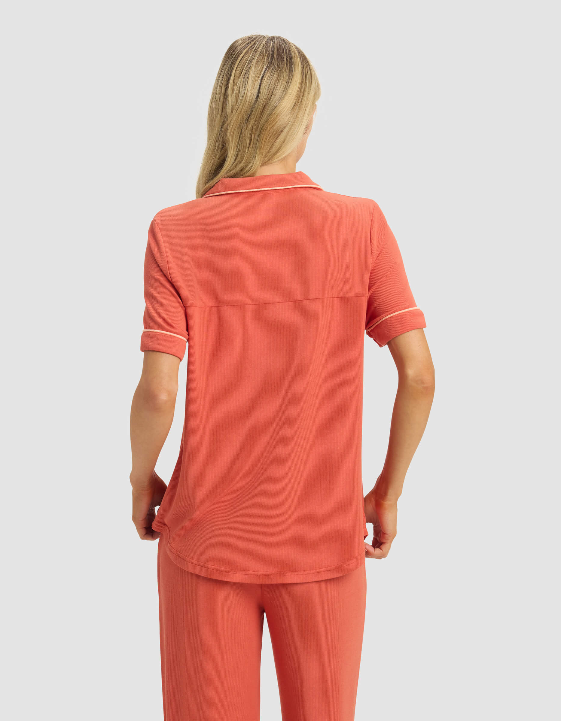 A woman with long blonde hair is shown from the back against a plain light gray background, wearing the Cozy Earth Women's Bamboo Rib-Knit Classic Short Sleeve Pajama Top in coral with matching pants.|Color:Sunset