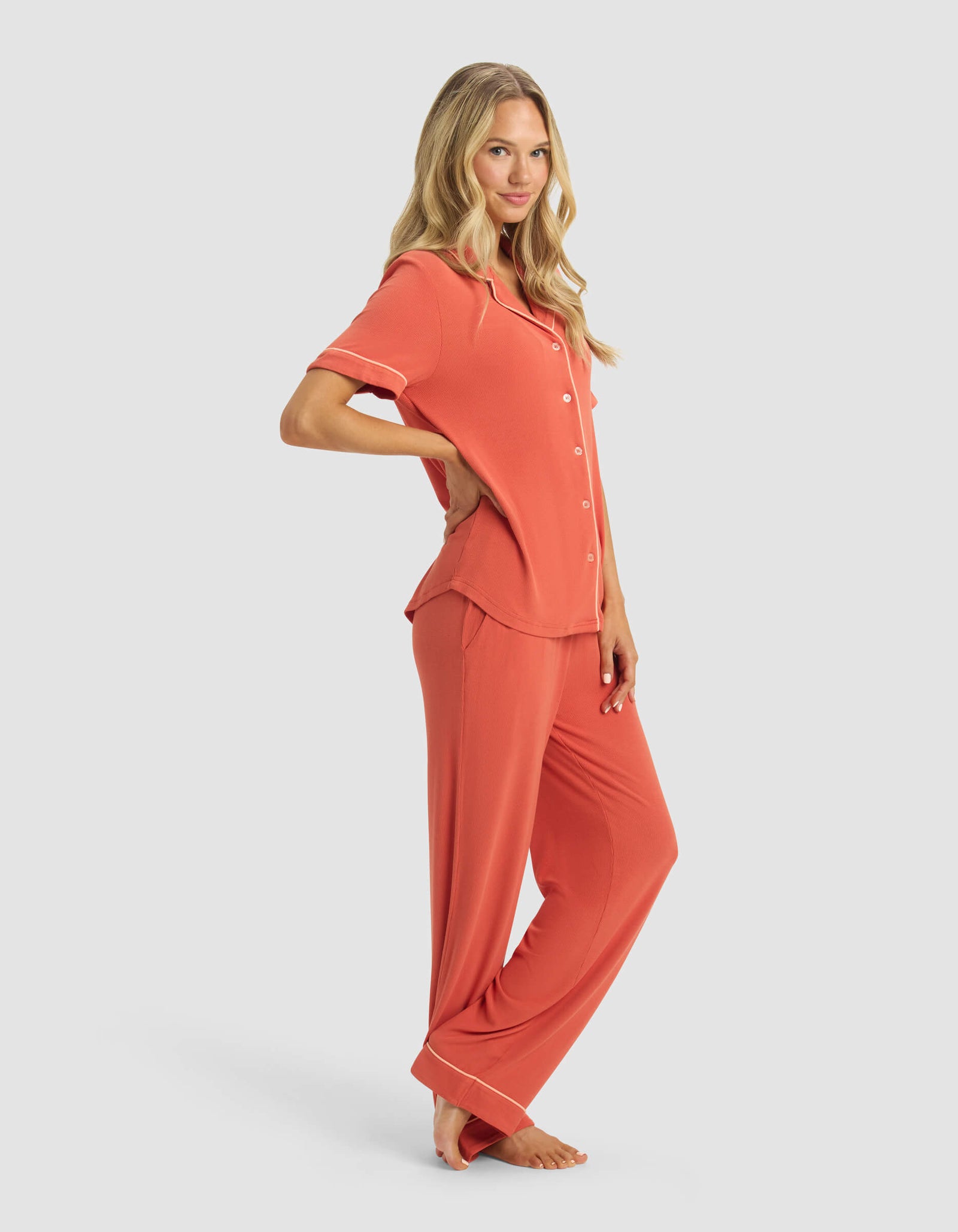 A woman stands barefoot in a relaxed pose wearing the Cozy Earth Women's Rib-Knit Classic Short Sleeve & Pant Pajama Set, featuring white piping, against a plain light gray background.