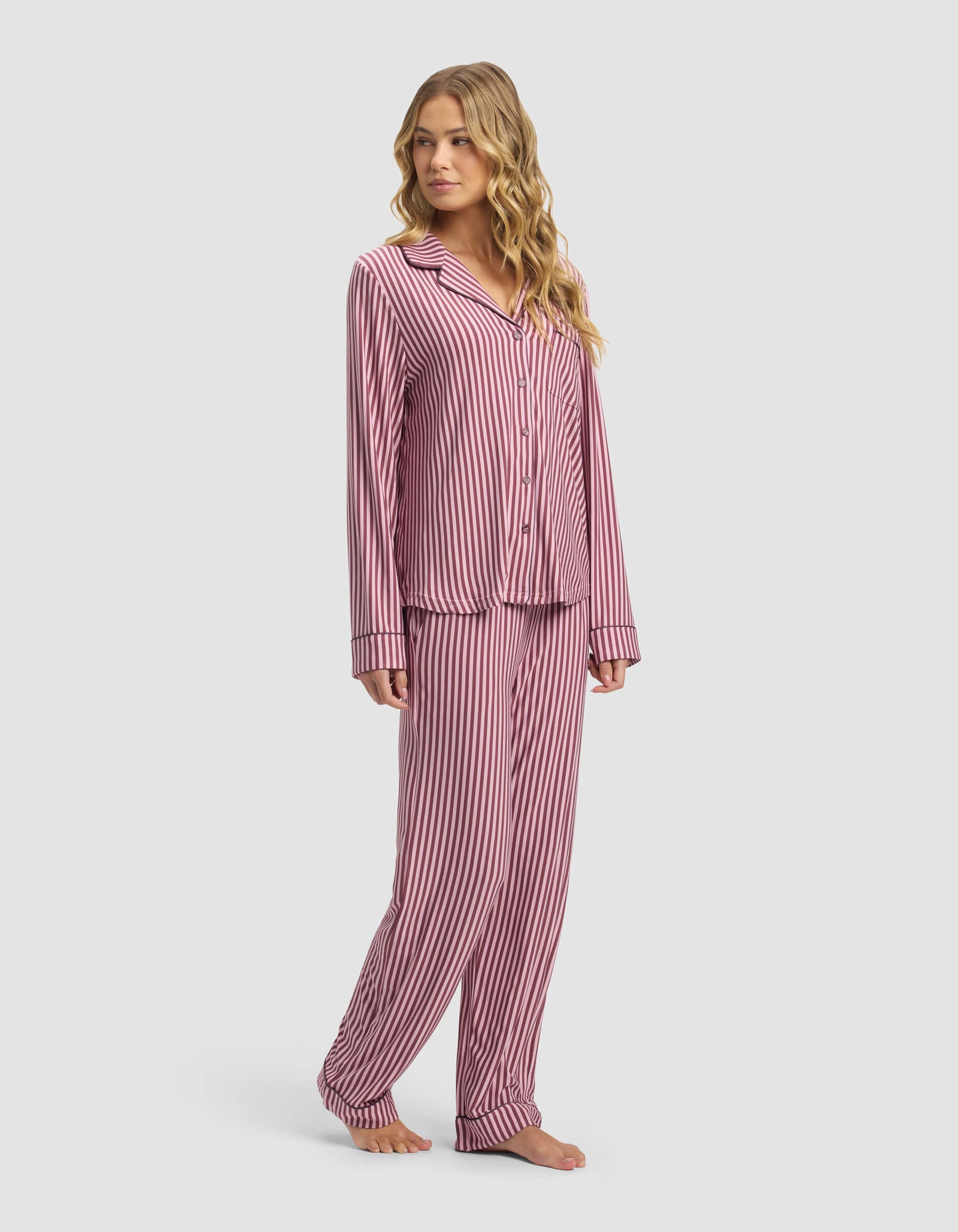 A woman stands barefoot against a plain light background wearing the Cozy Earth Women's Bamboo Stretch-Knit Long Sleeve Pajama Set with vertical pink and white stripes.