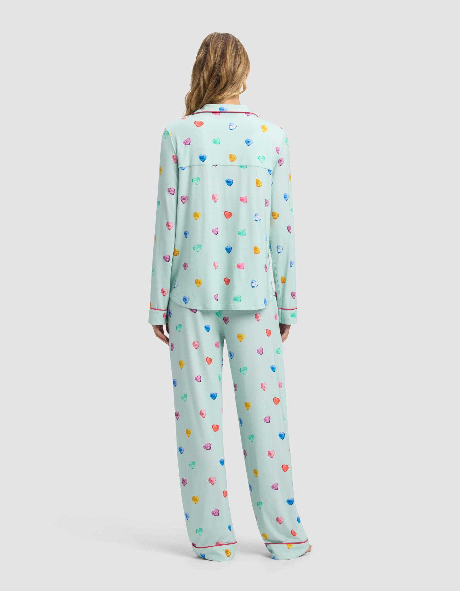 A person with long hair wears the Cozy Earth Women's Bamboo Stretch-Knit Long Sleeve Pajama Set in light blue with multicolored hearts, shown from the back against a plain light gray background.