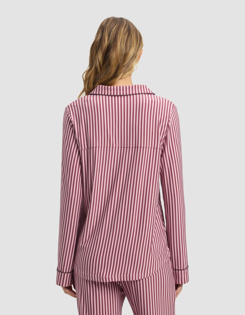 A person with wavy hair is shown from the back wearing the Cozy Earth Women's Bamboo Stretch-Knit Long Sleeve Pajama Top in pink and white stripes, paired with matching pants, against a plain light background.