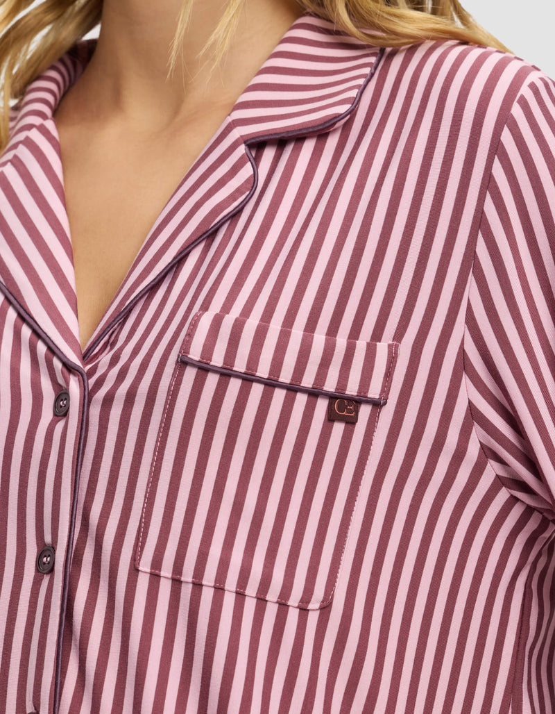 A close-up of a person wearing the Cozy Earth Women's Bamboo Stretch-Knit Long Sleeve Pajama Top in pink and burgundy stripes, featuring a front chest pocket with a small metal tag and a collared, button-up design.