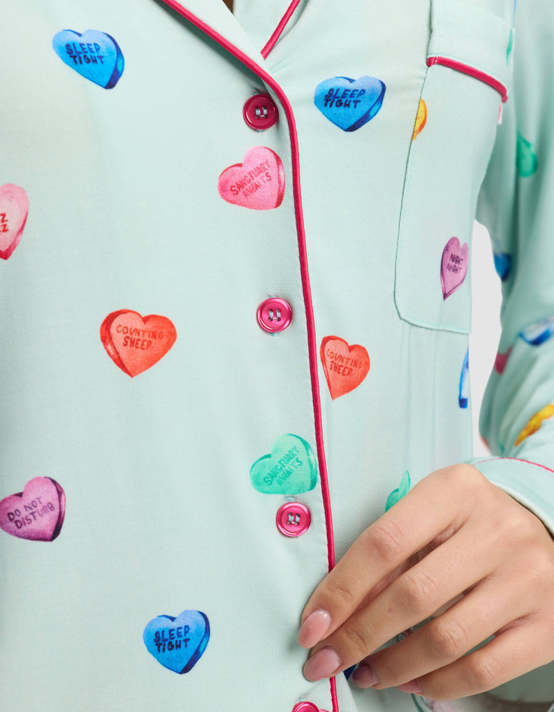 A close-up of a person wearing Cozy Earth’s Women's Bamboo Stretch-Knit Long Sleeve Pajama Top in light blue, featuring pink piping and colorful heart-shaped designs with phrases like "SWEETHEART" and "COUNTING SHEEP.