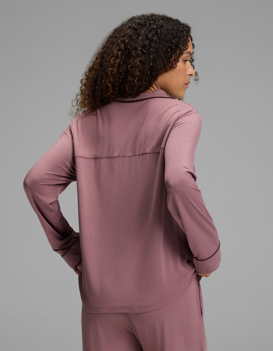 A woman wears a mauve Women’s Bamboo Stretch-Knit Long Sleeve Pajama Top - Petite with a collared neckline and dark piping detail, viewed from behind.