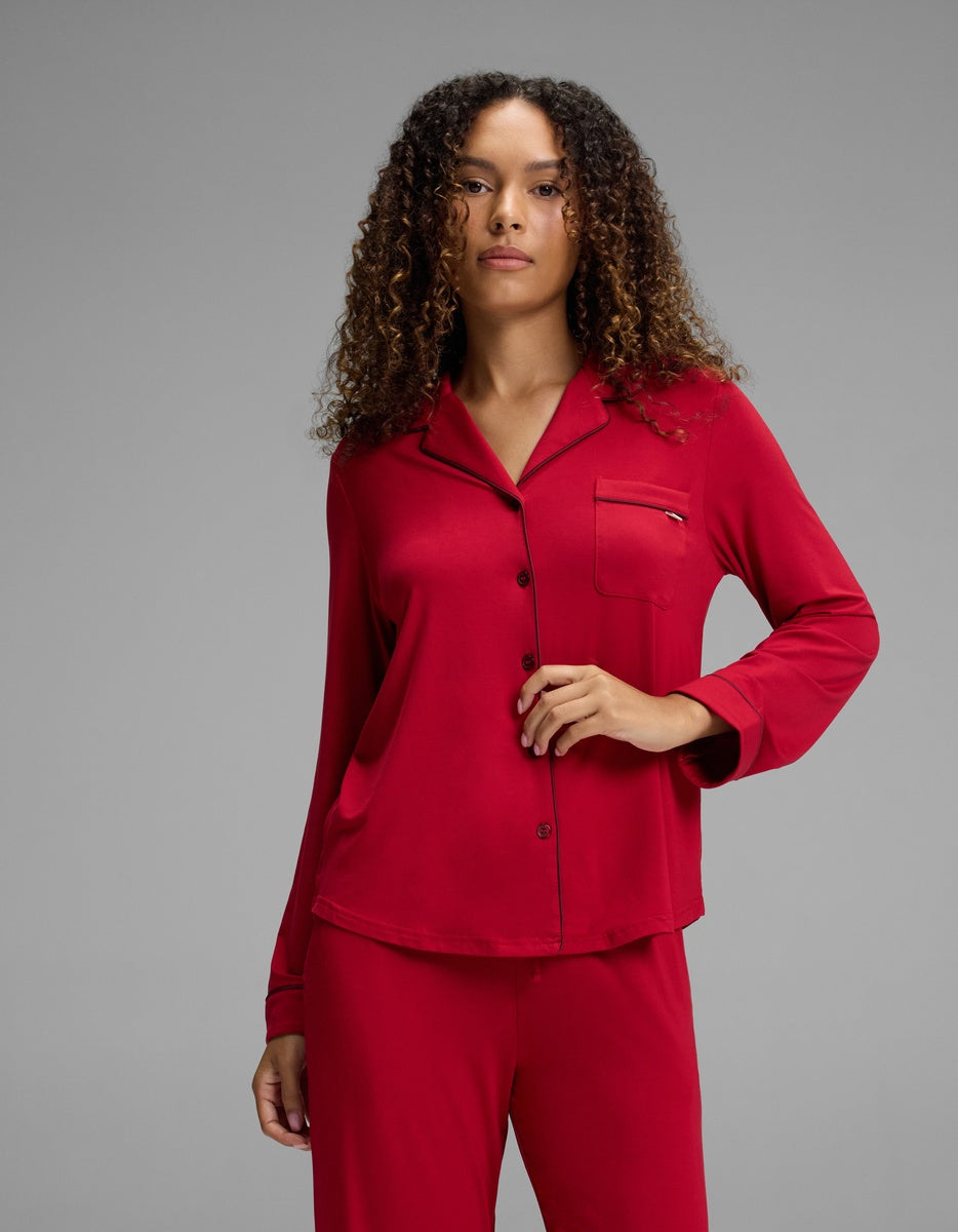 A woman wearing a red Cozy Earth Women’s Bamboo Stretch-Knit Long Sleeve Pajama Top, featuring a notched collar, chest pocket, and dark piping.
