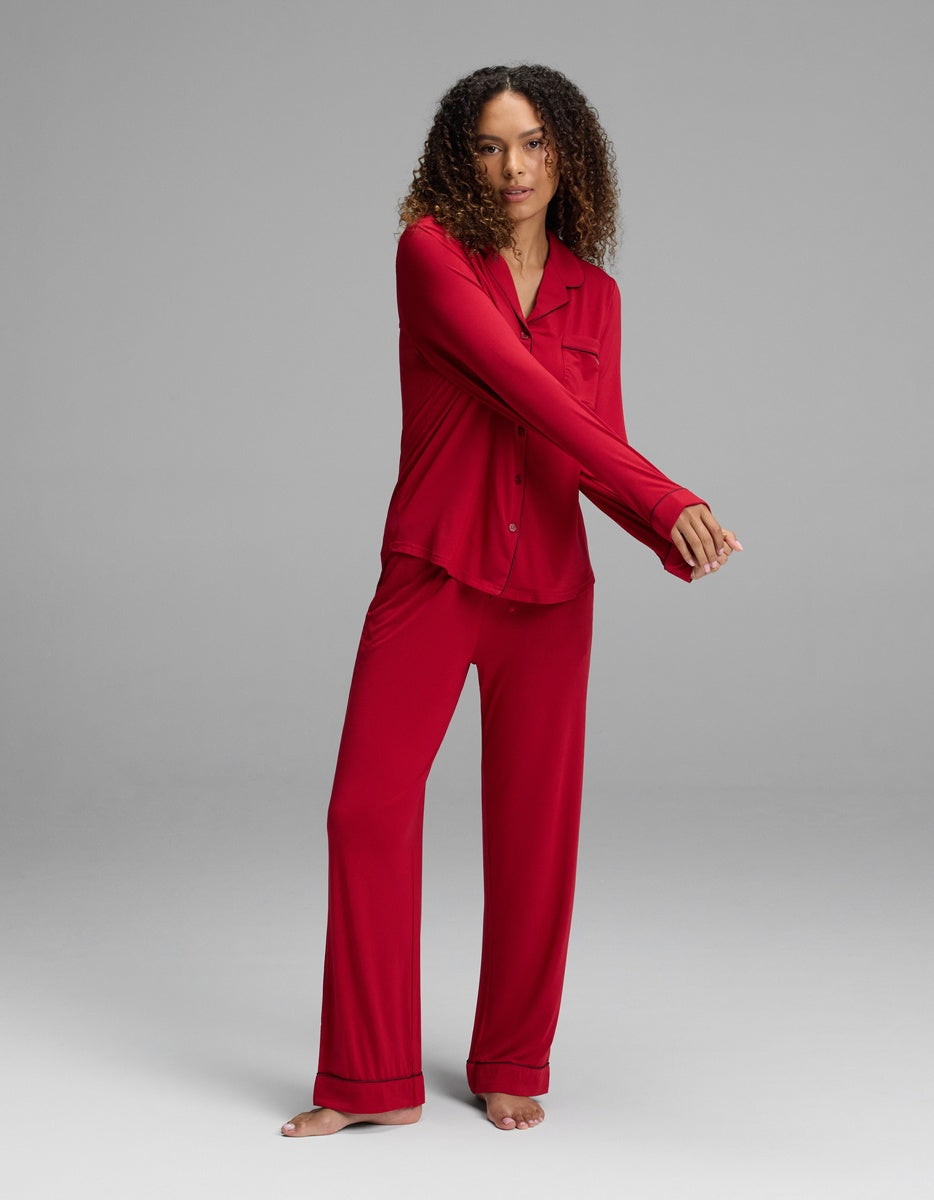 A woman wearing a red Women’s Bamboo Stretch-Knit Long Sleeve Pajama Top and matching pajama pants with black piping.