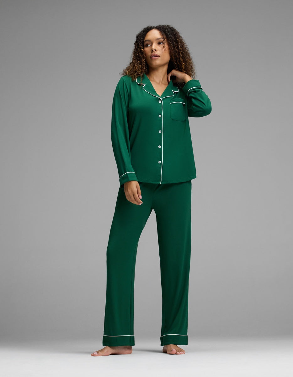 A person wearing a forest green Women’s Bamboo Stretch-Knit Long Sleeve Pajama Top and matching pants with white piping.