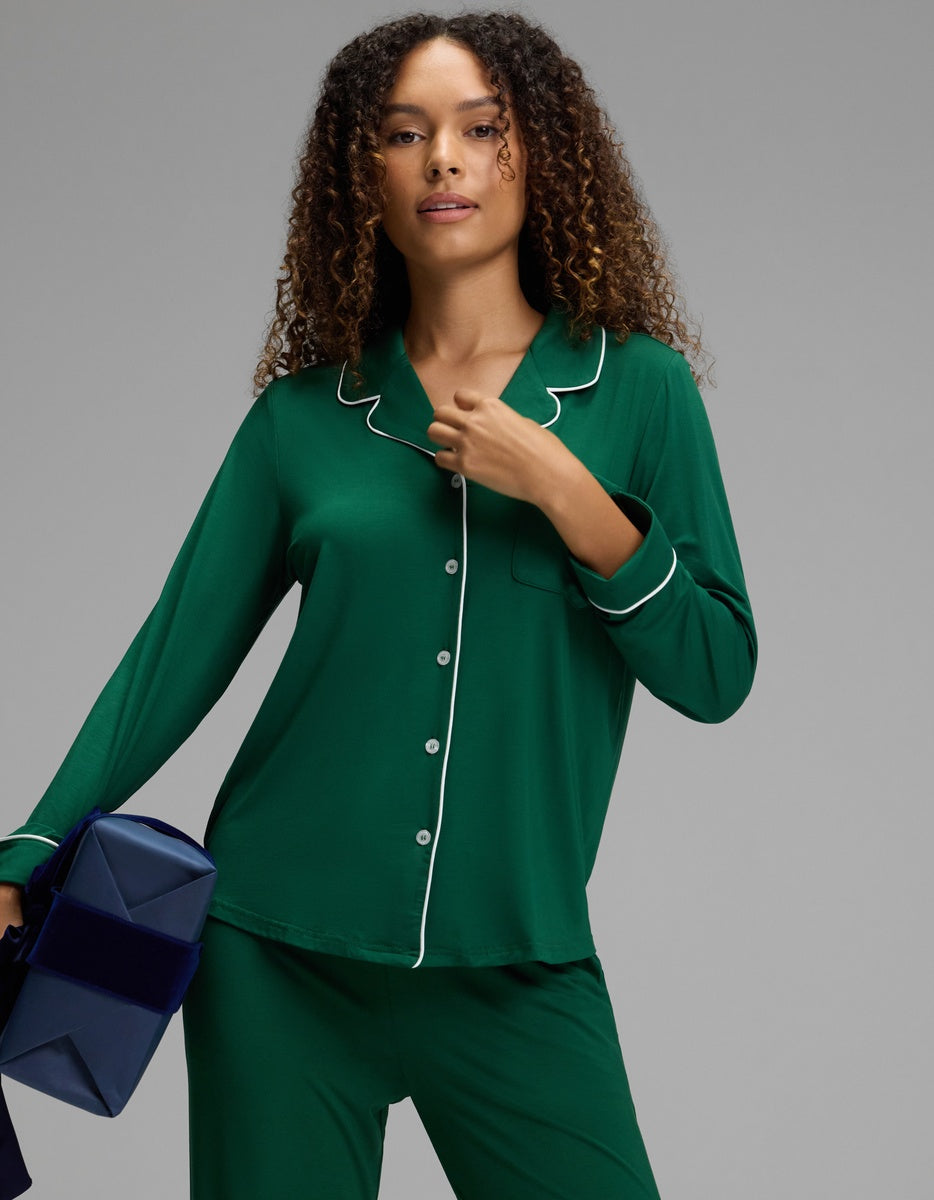 A person wearing a green, long-sleeved Cozy Earth Women’s Bamboo Stretch-Knit Long Sleeve Pajama Top with white piping trim.