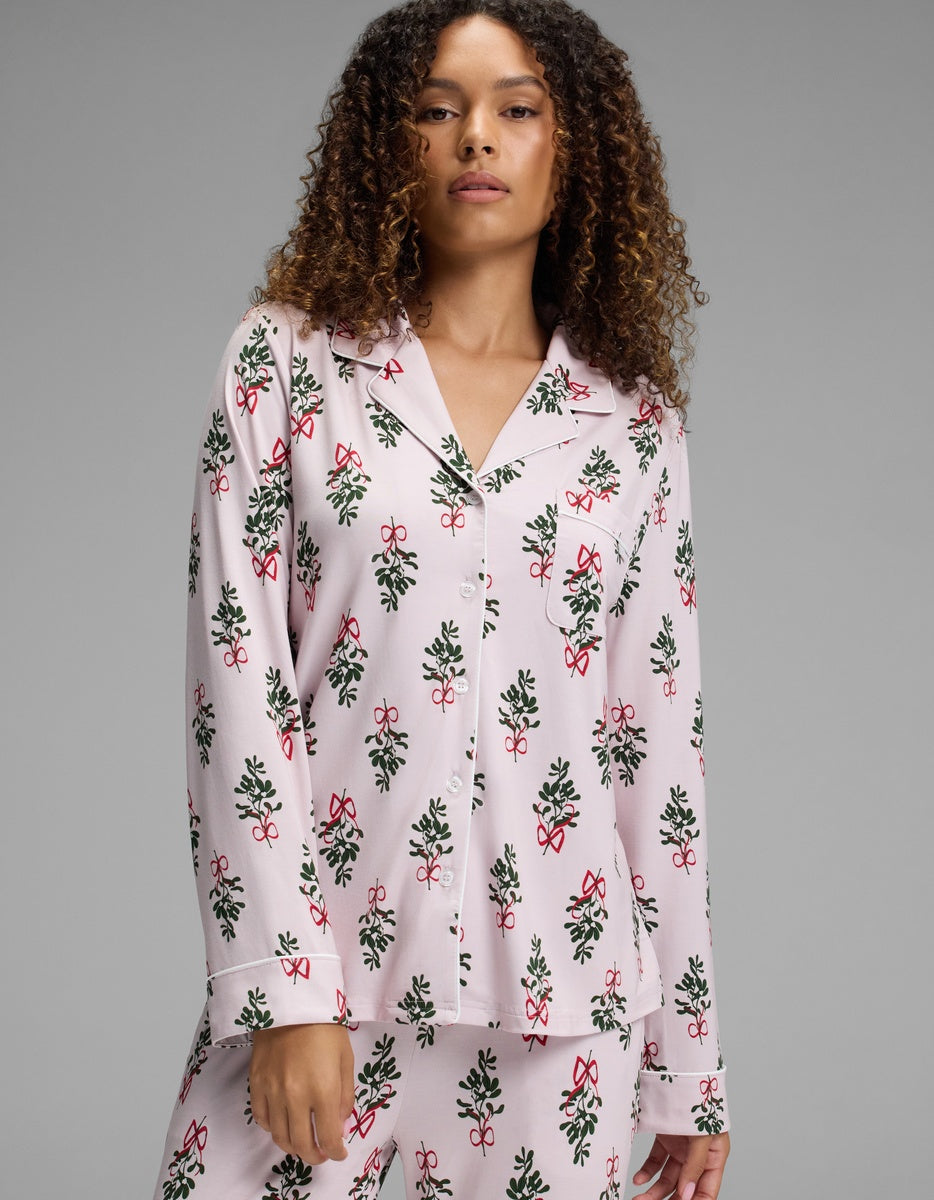 A woman wears a pale pink Cozy Earth Women’s Bamboo Stretch-Knit Long Sleeve Pajama Top featuring a repeating pattern of green holly branches and red berries.