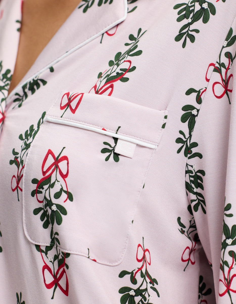Cozy Earth Women’s Bamboo Stretch-Knit Long Sleeve Pajama Top in pale pink with a mistletoe and red ribbon print, featuring white piping trim on the collar and chest pocket.