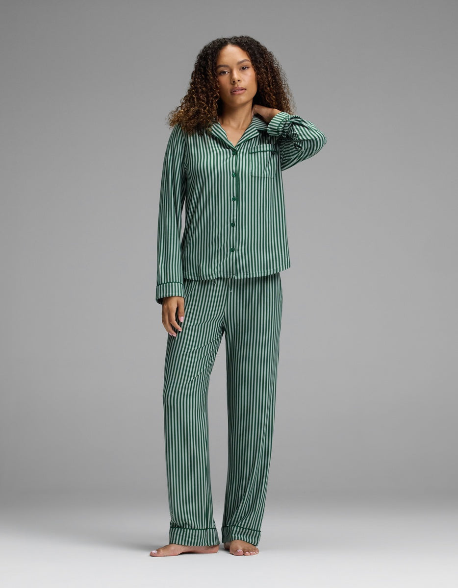 A woman wearing a Cozy Earth Women’s Bamboo Stretch-Knit Long Sleeve Pajama Top and matching pants in dark green and black stripes.