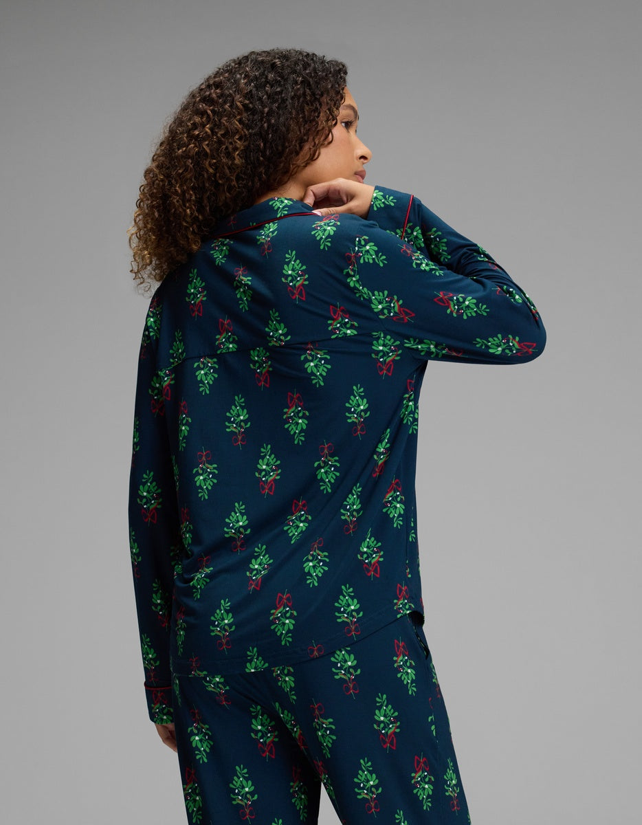 View from behind of a woman wearing a dark blue Cozy Earth Women’s Bamboo Stretch-Knit Long Sleeve Pajama Top with a green and red holiday-themed print and red piping.