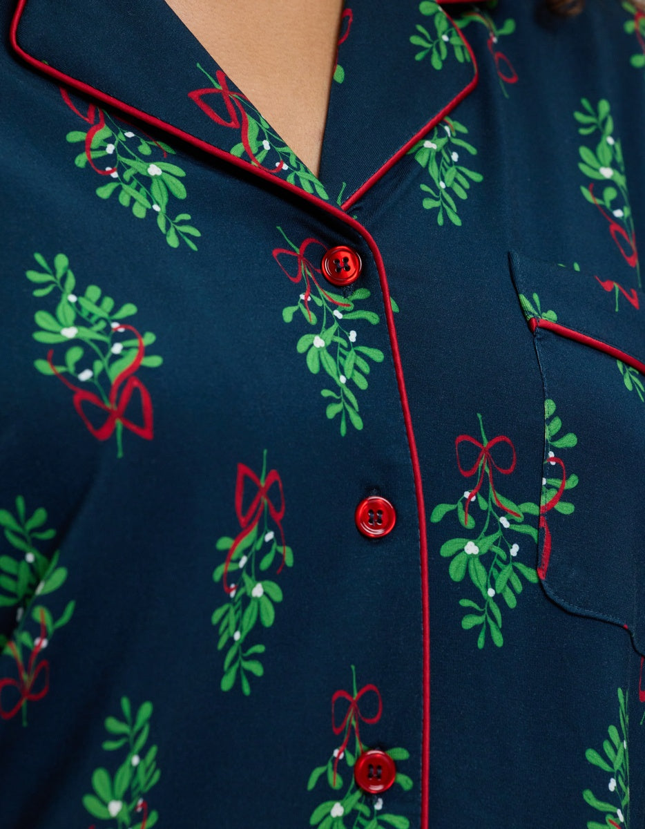 Cozy Earth Women’s Bamboo Stretch-Knit Long Sleeve Pajama Top in navy blue with a mistletoe and red ribbon print, featuring a notched collar and red piping trim.