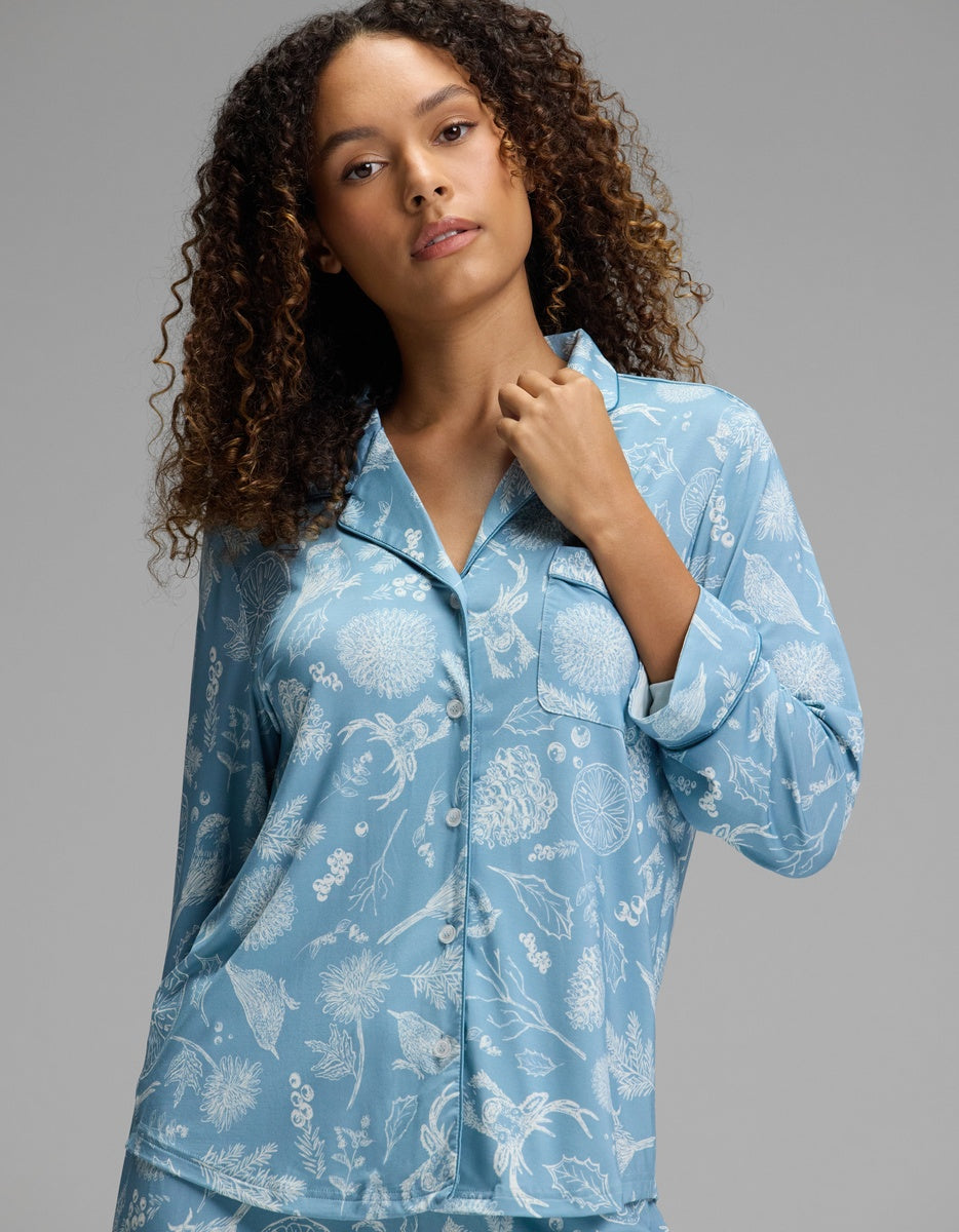 A woman wears a light blue, long-sleeved Cozy Earth Women’s Bamboo Stretch-Knit Long Sleeve Pajama Top with a white botanical print.