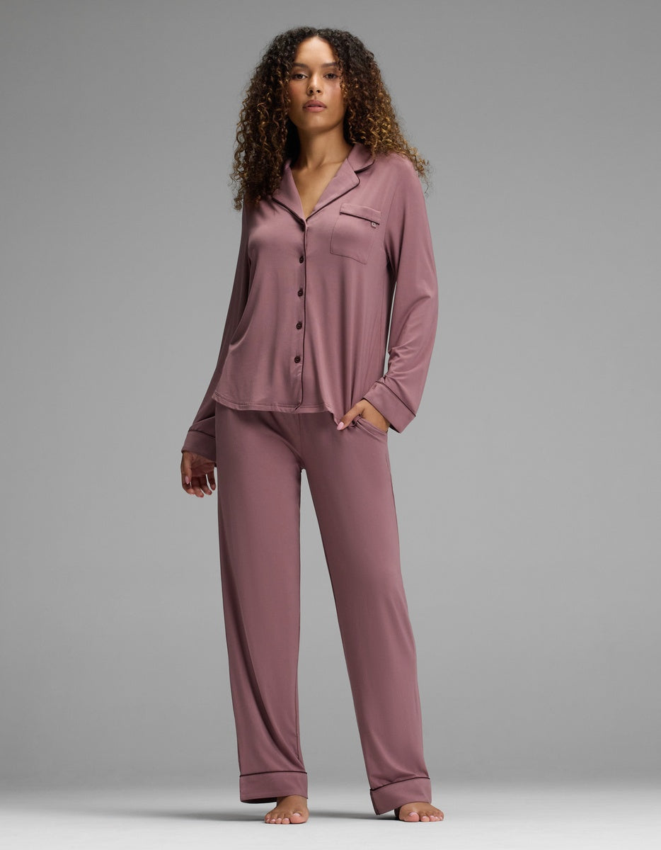 A woman wears a copper rose Women’s Bamboo Stretch-Knit Long Sleeve Pajama Set - Petite featuring a long-sleeve, button-down top with a notch collar and matching pants.