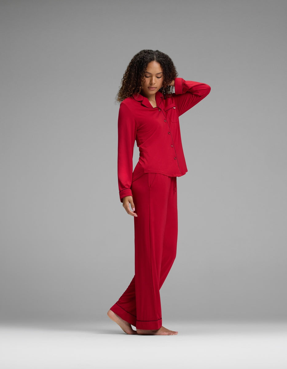 A person wearing a deep red Women’s Bamboo Stretch-Knit Long Sleeve Pajama Set with dark trim, featuring a long-sleeved, button-down top and matching full-length pants.