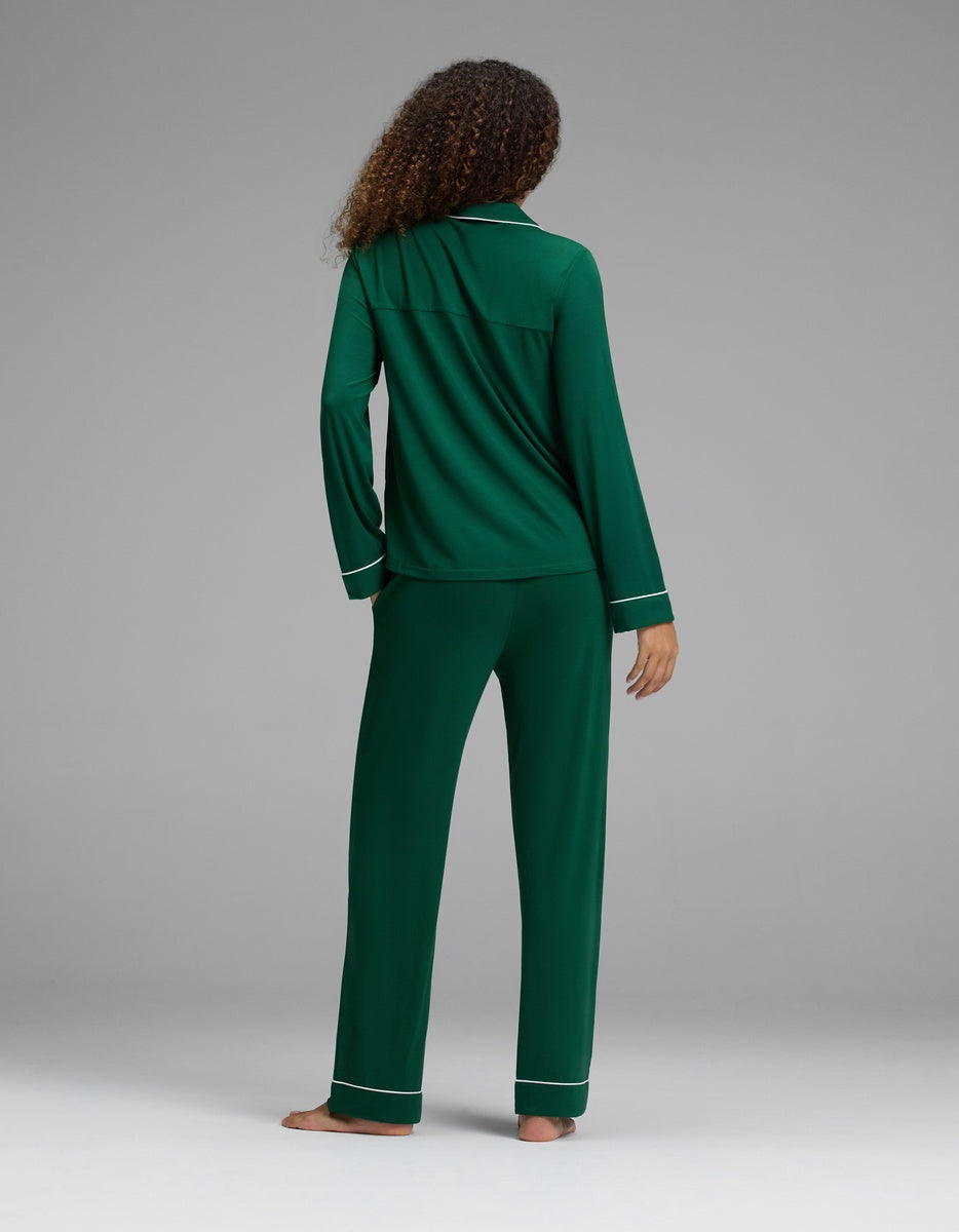 A person seen from behind wearing a forest green Women’s Bamboo Stretch-Knit Long Sleeve Pajama Set with white piping trim.