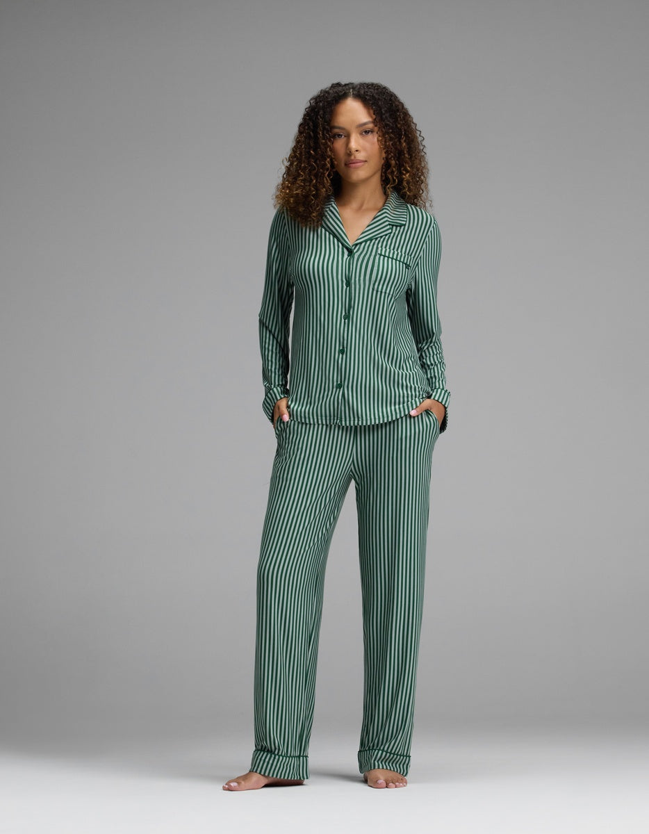 A person wearing a dark green and black vertically striped Cozy Earth Women’s Bamboo Stretch-Knit Long Sleeve Pajama Set, featuring a long-sleeved button-down top and matching straight-leg pants.
