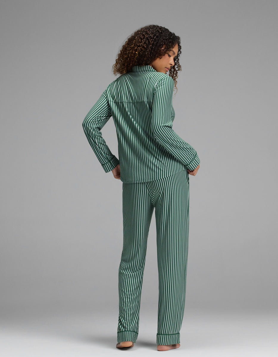 A person seen from behind, wearing a Women’s Bamboo Stretch-Knit Long Sleeve Pajama Set with dark green and light green vertical stripes on the long-sleeved button-down top and matching pants.