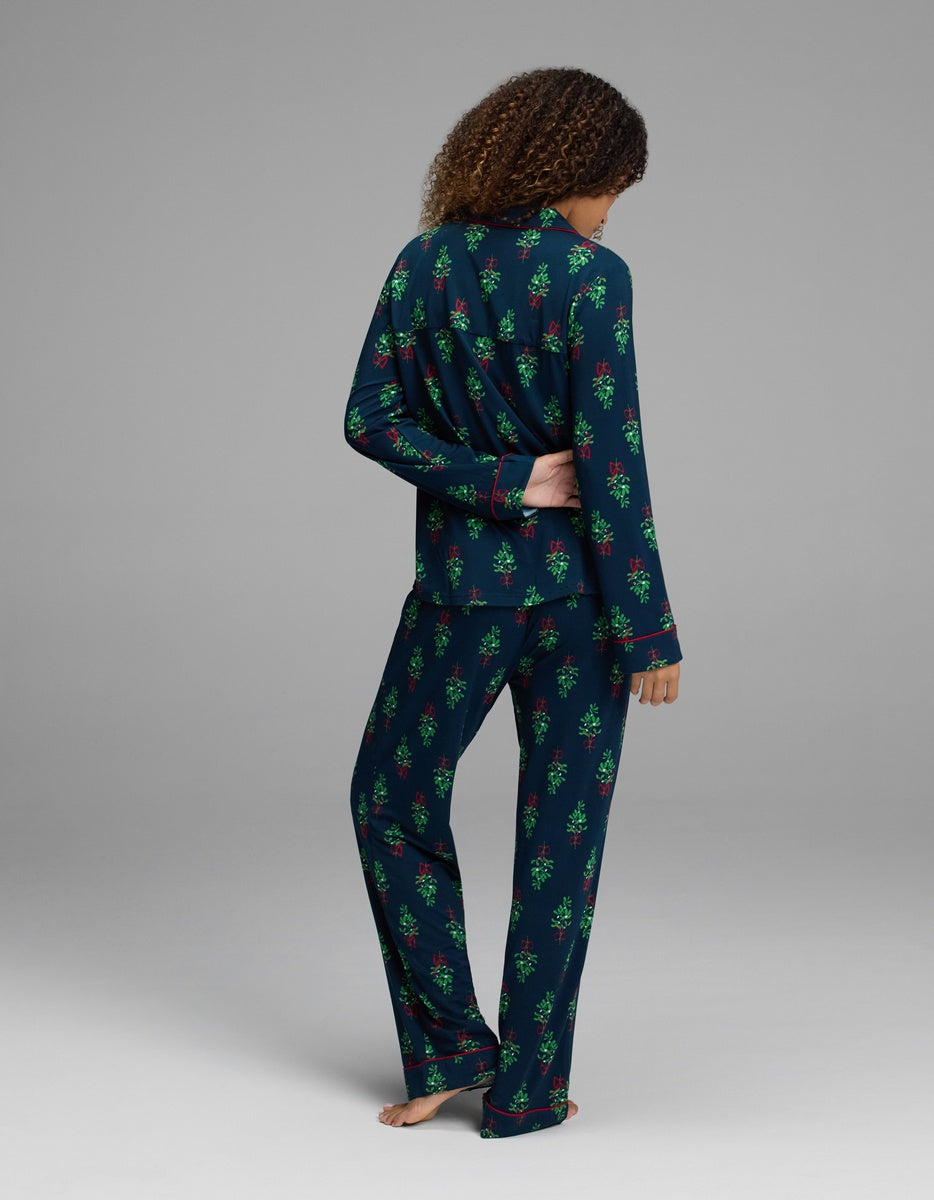 A person wearing a Cozy Earth Women’s Bamboo Stretch-Knit Long Sleeve Pajama Set in dark blue with a red and green mistletoe pattern and red piping.