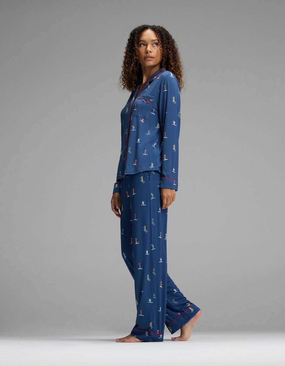 A woman wearing a Cozy Earth Women’s Bamboo Stretch-Knit Long Sleeve Pajama Set in navy blue with a skier pattern and red trim.