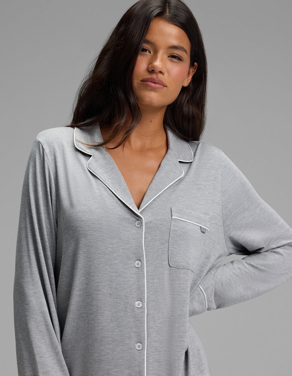 A person wears a grey Cozy Earth Women’s Bamboo Stretch-Knit Long Sleeve Sleep Dress featuring a button-up front, notched lapels, and white piping trim.