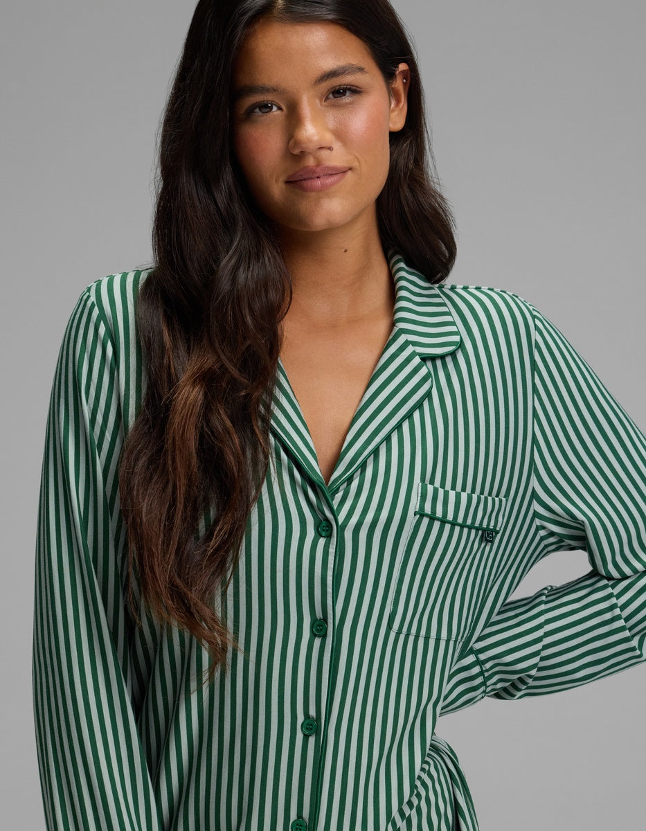 A woman wearing a Cozy Earth Women’s Bamboo Stretch-Knit Long Sleeve Sleep Dress featuring a green and white vertical stripe pattern, long sleeves, a button-down front, and a notched collar.