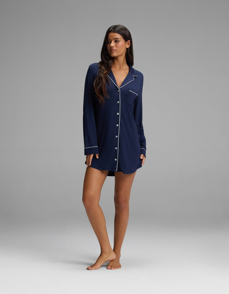 A person wearing a navy blue long-sleeved Women’s Bamboo Stretch-Knit Long Sleeve Sleep Dress with white piping detail.