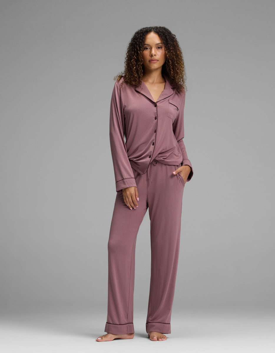 A woman wears a mauve long-sleeved button-down pajama top and matching Women’s Bamboo Stretch-Knit Pajama Pant - Petite.