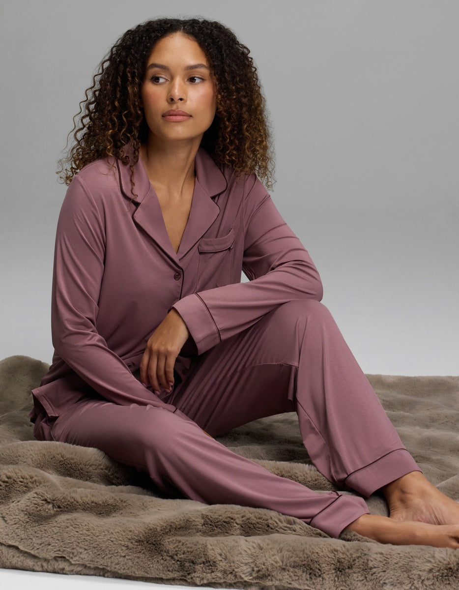 A woman wearing a mauve long-sleeved top and matching Women’s Bamboo Stretch-Knit Pajama Pant, sitting on a soft surface.
