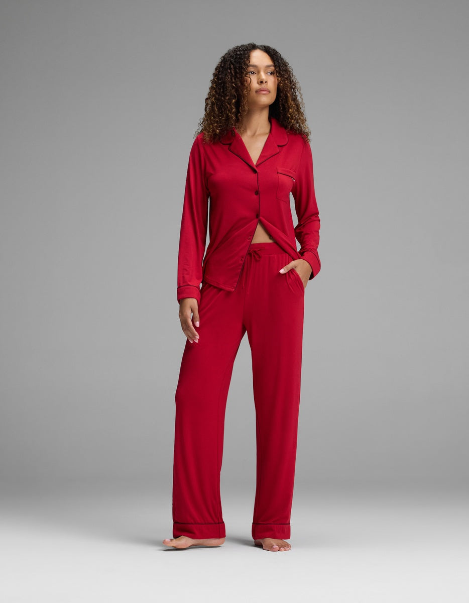 A woman wearing a red long-sleeved button-down pajama top and matching Women’s Bamboo Stretch-Knit Pajama Pant with a drawstring waist.