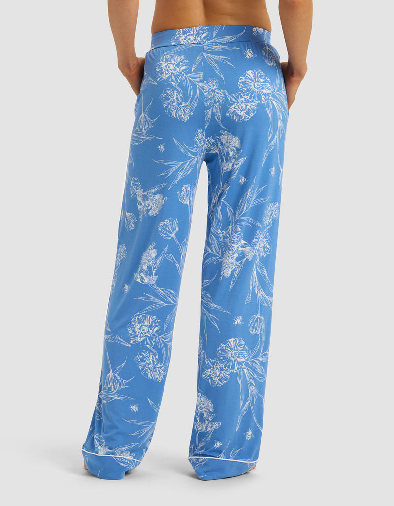 A person faces away, wearing Cozy Earth Women's Bamboo Stretch-Knit Pajama Pant in blue with a white floral pattern, hands at their sides, against a plain background.