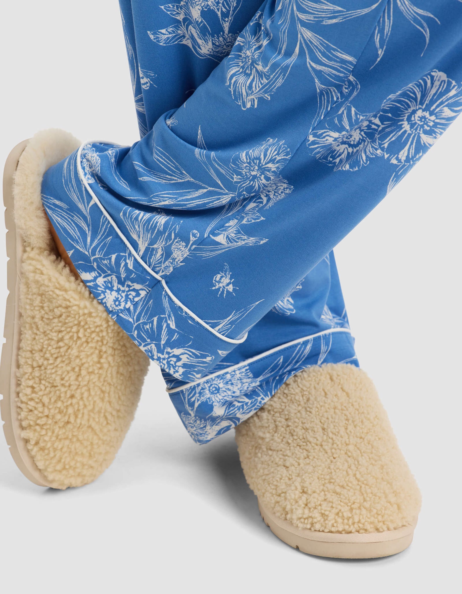 A person wearing Cozy Earth Women's Bamboo Stretch-Knit Pajama Pant and beige fuzzy slippers stands with their legs crossed at the ankles against a plain background.