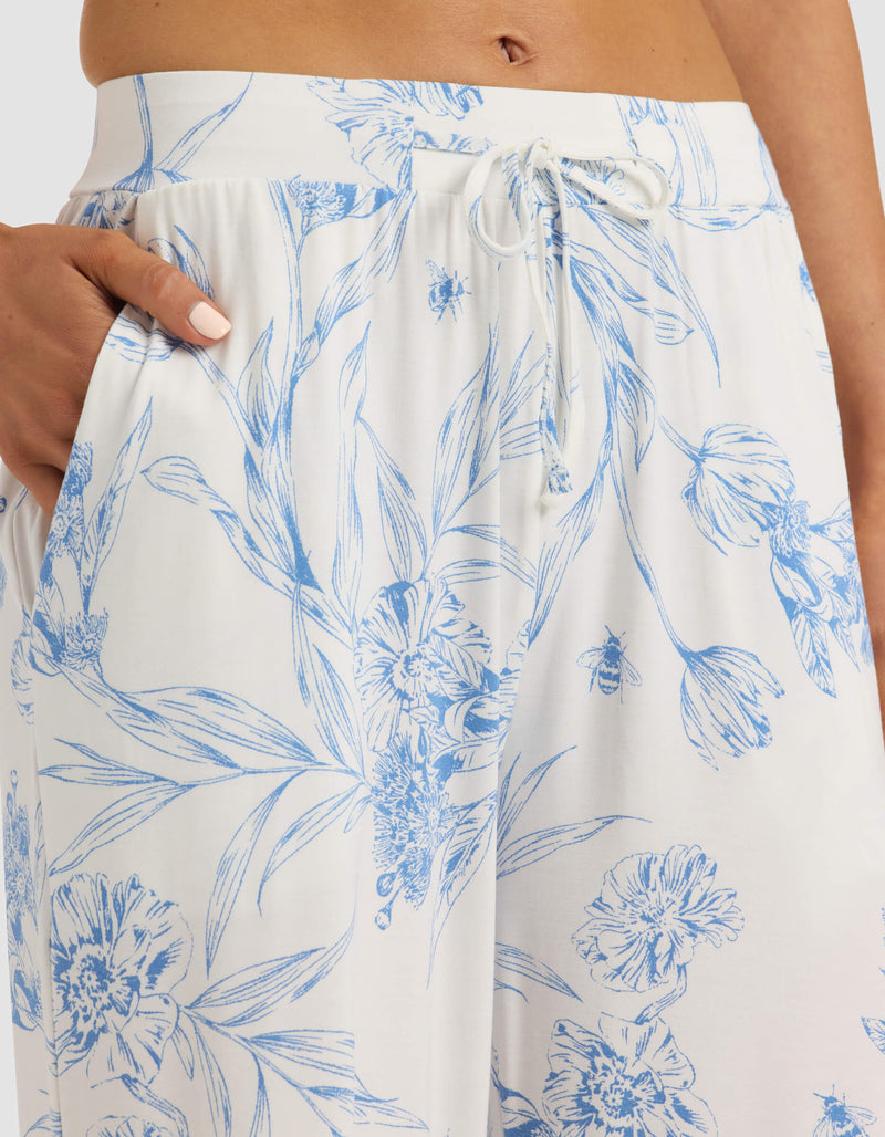 A person wears Cozy Earth’s Women's Bamboo Stretch-Knit Pajama Pant, featuring a blue floral print, drawstring waist, and relaxed fit.